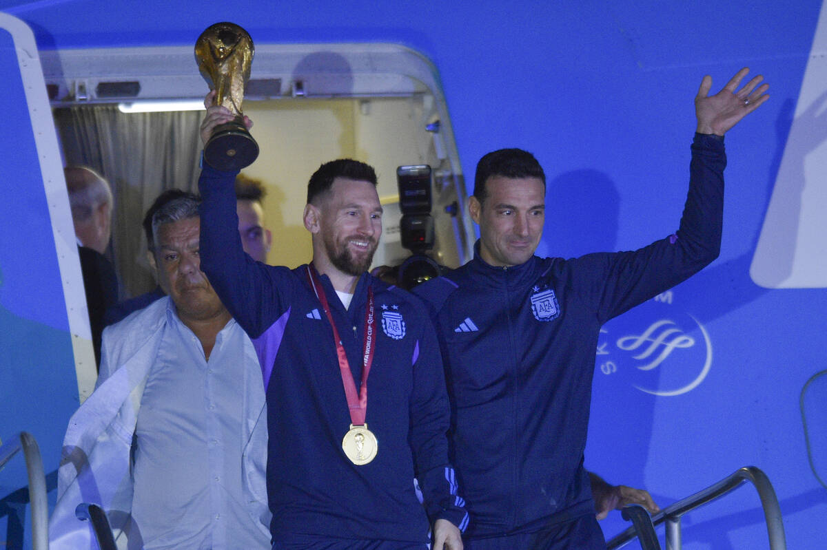 Argentina's Lionel Messi holds the FIFA World Cup trophy as he deplanes, with coach Lionel Scal ...