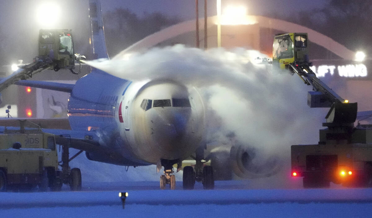 An American Airlines plane is de-iced as high winds whip around 7.5 inches of new snow at Minne ...