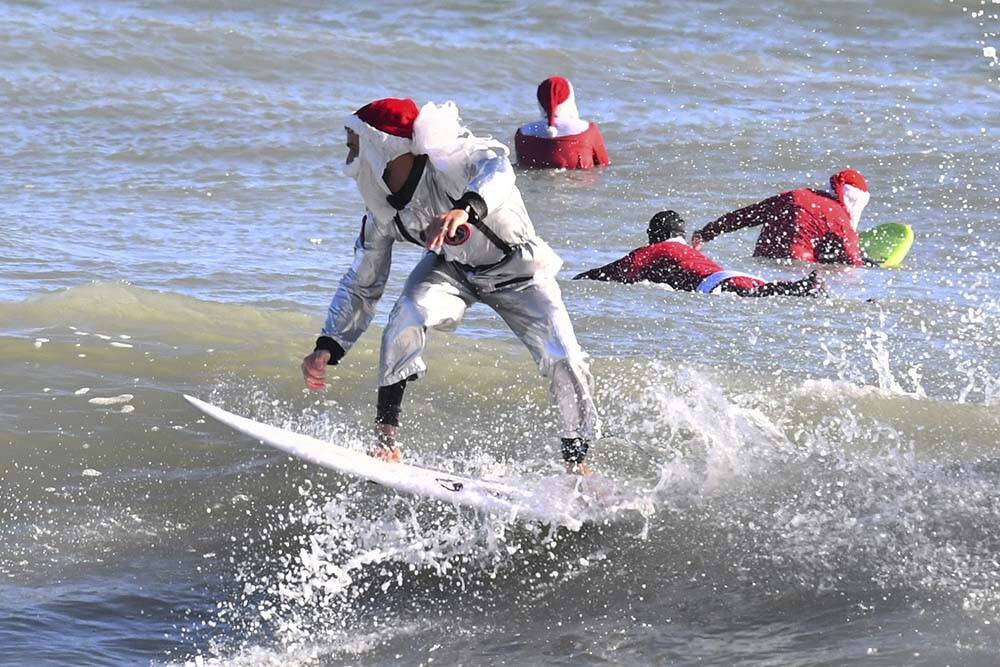 Surfer Corey Howell in a space man Surfing Santa suit, rides with waves with other surfing Sant ...