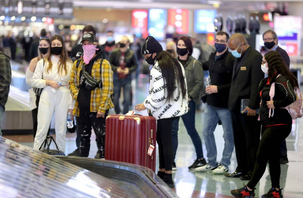 Masked travelers retrieve their luggage in baggage claim Terminal 1 at the airport in Las Vegas ...