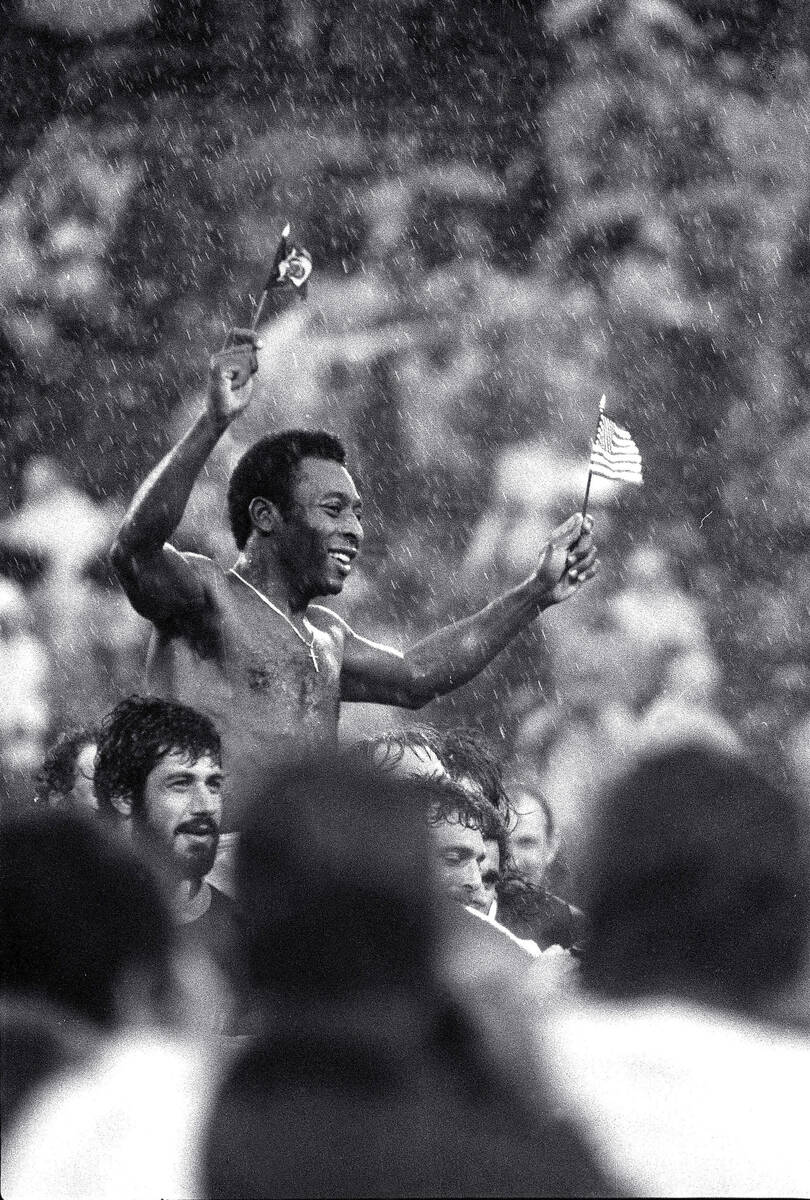 Soccer superstar Pele, waving the flags of Brazil and the U.S., is carried off the field in dri ...