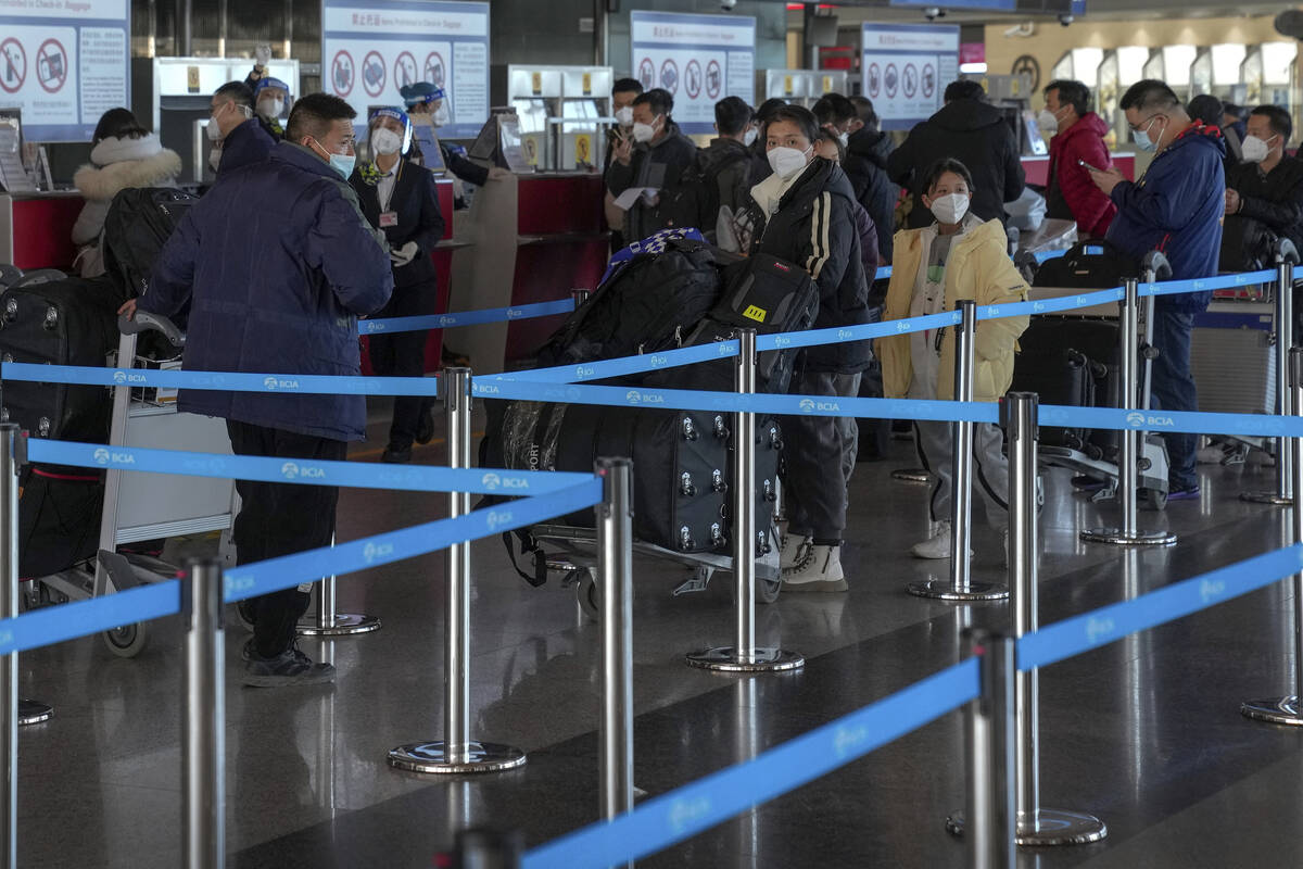 Masked travellers with luggage line up at the international flight check in counter at the Beij ...