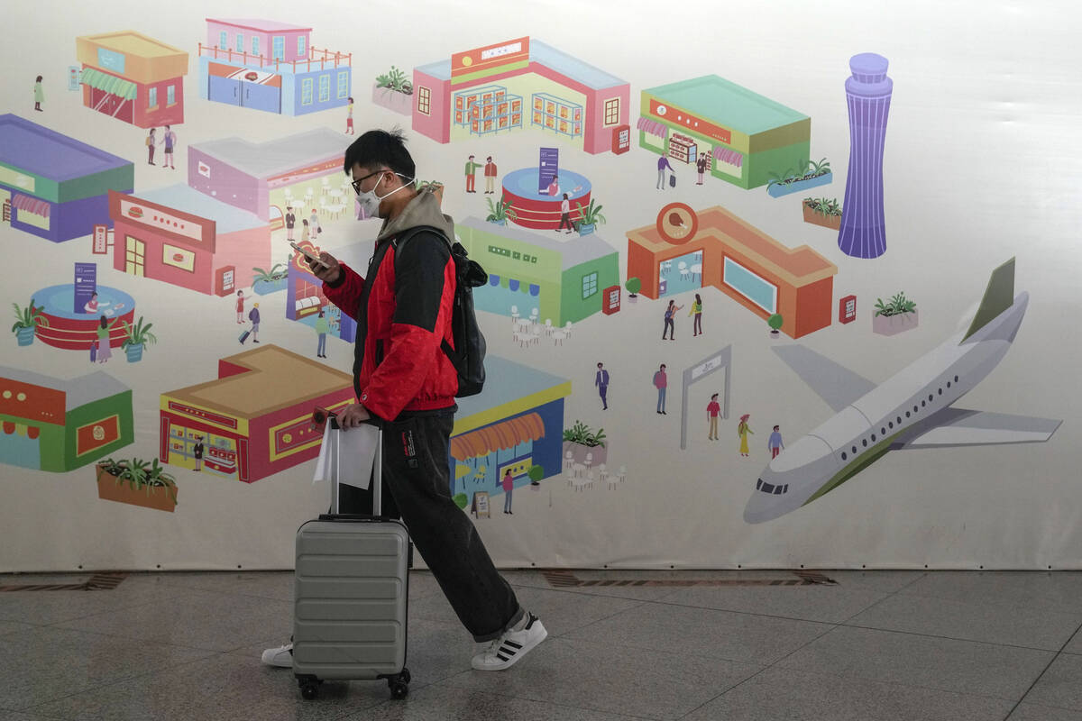 A traveller wearing a face mask with his luggage and passport walks by a poster depicting the B ...