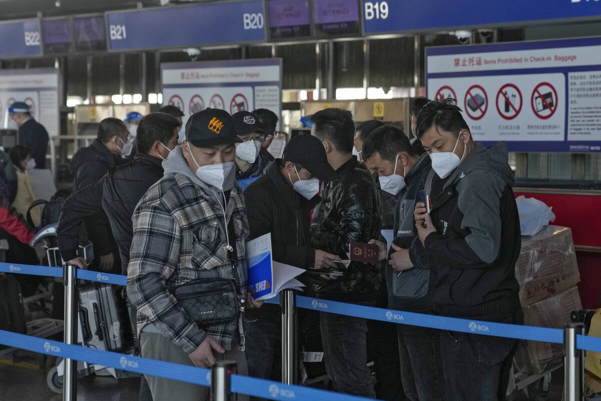 Masked travellers check their passports as they line up at the international flight check in co ...