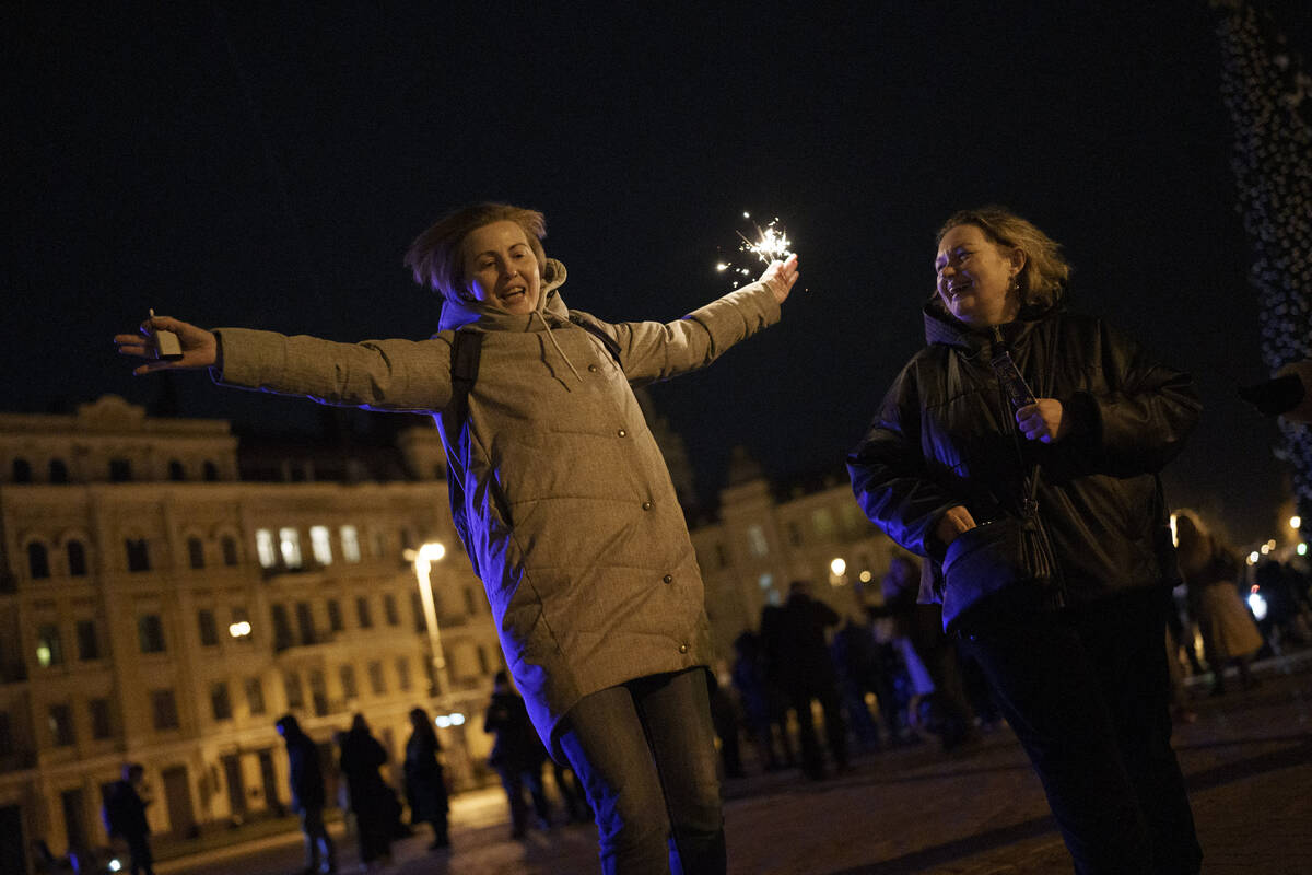 A woman holds a sparkler as she dances in Sophia Square before curfew on New Year's Eve in Kyiv ...