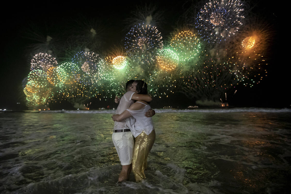 People celebrate the start of the New Year, backdropped by fireworks exploding in the backgroun ...