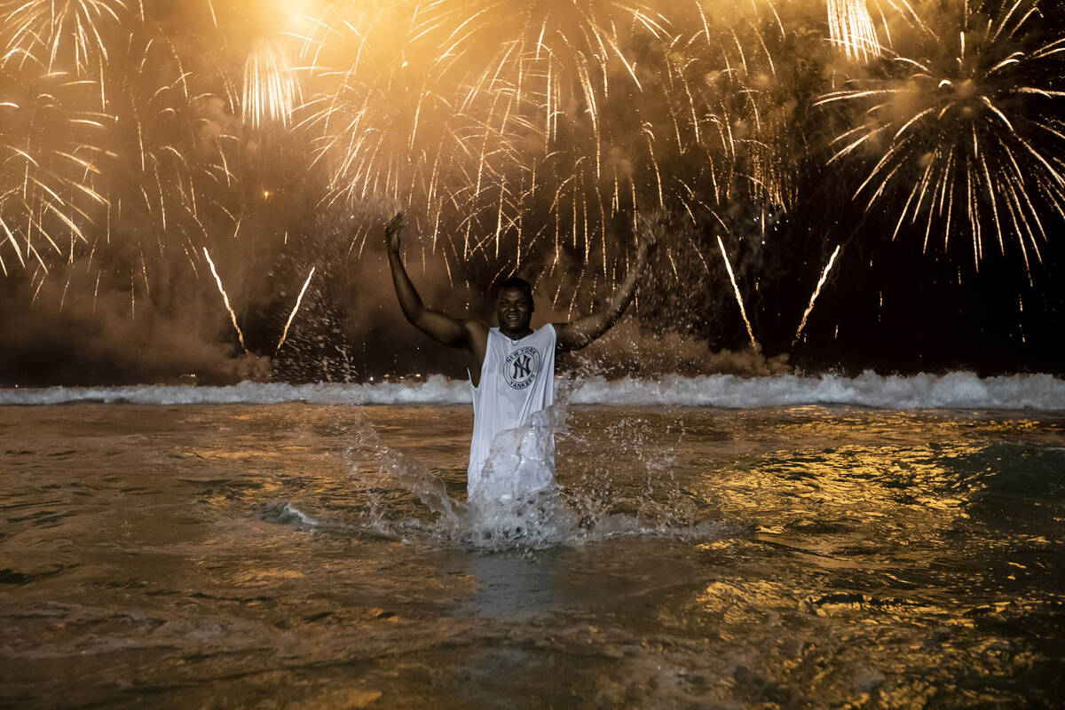 A man celebrates the start of the New Year, backdropped by fireworks exploding in the backgroun ...