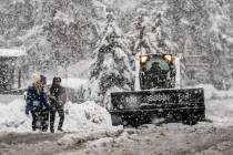 Pedestrians walk along a road as a snow plow works in South Lake Tahoe, Calif., Saturday, Dec. ...