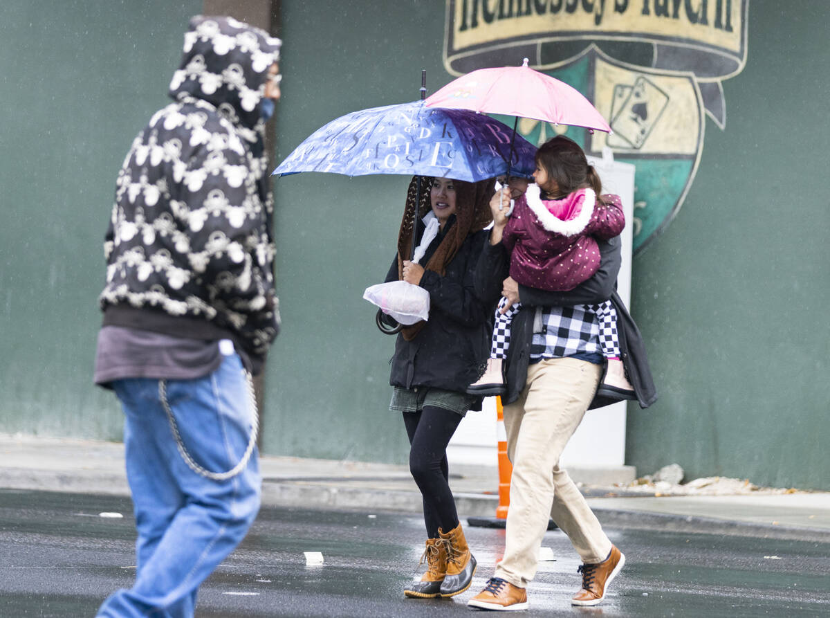 Pedestrians hold umbrellas to protect themselves from rain as they cross Fremont Street during ...
