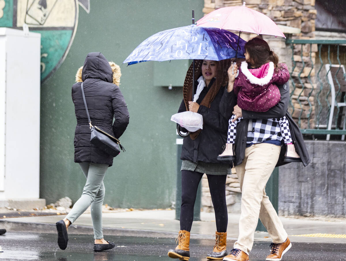 Pedestrians hold umbrellas to protect themselves from rain as they cross Fremont Street during ...