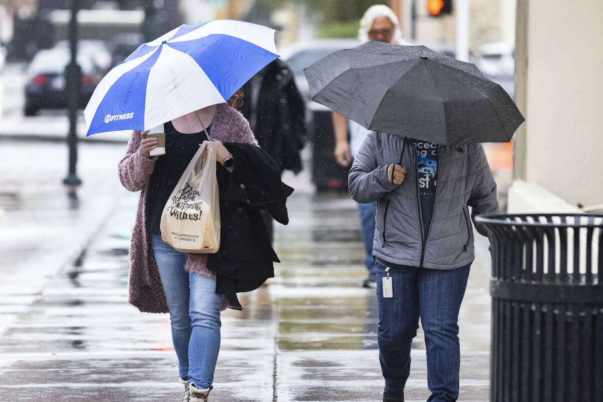 Pedestrians hold umbrellas to protect themselves from rain as they walk along Lewis Avenue duri ...