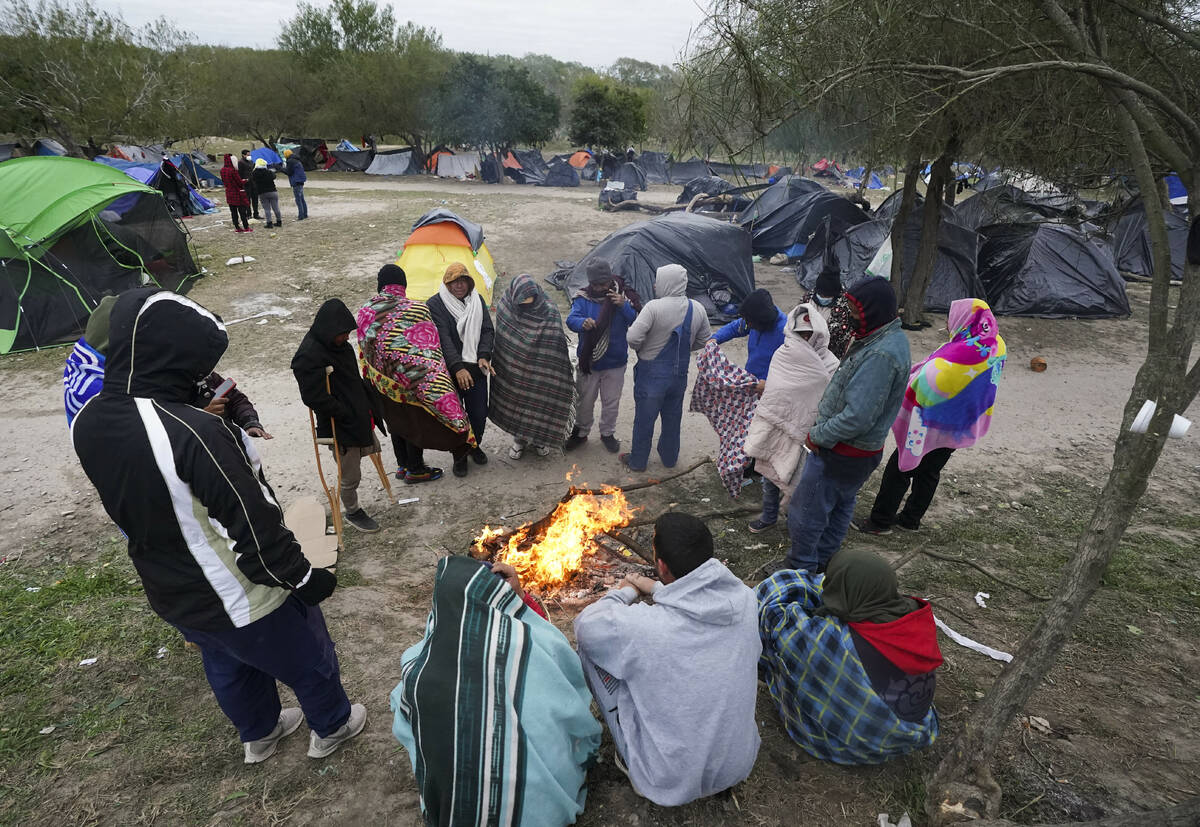 FILE - Migrants stand in the cold weather around a campfire at a makeshift camp on the U.S.-Mex ...