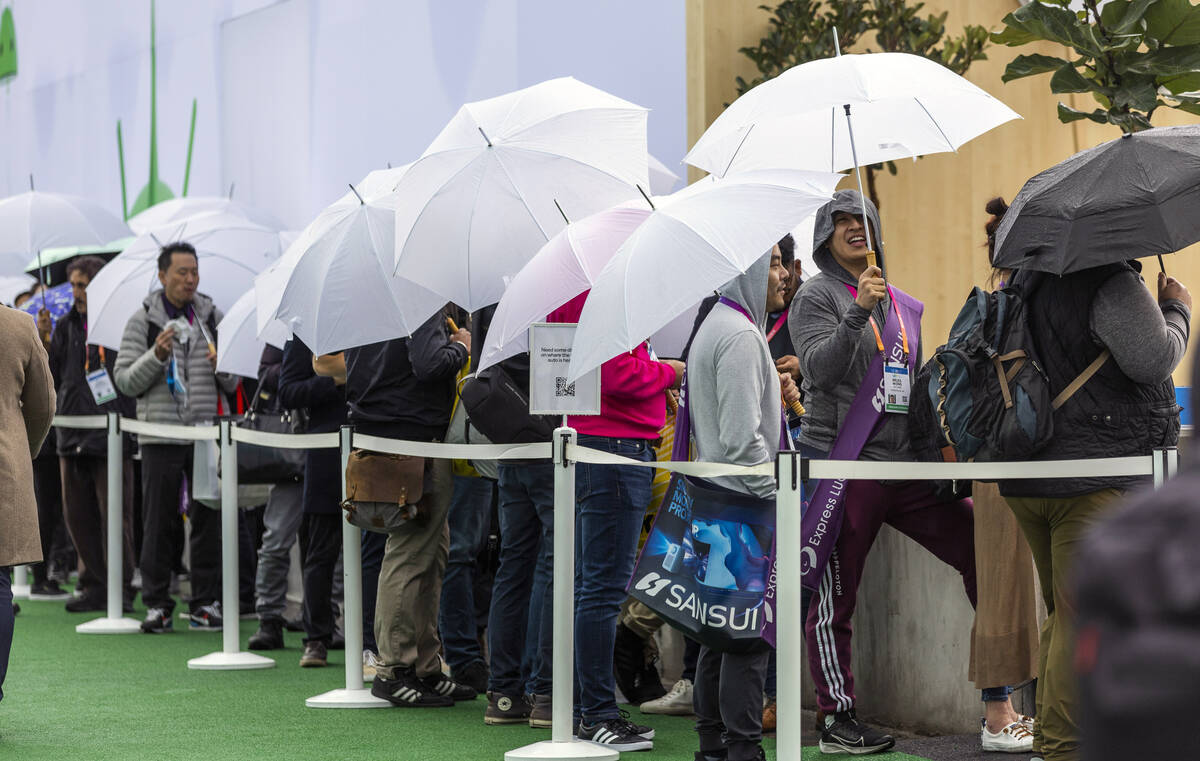 Attendees stay dry from the rain under umbrellas outside the Google display space during the op ...