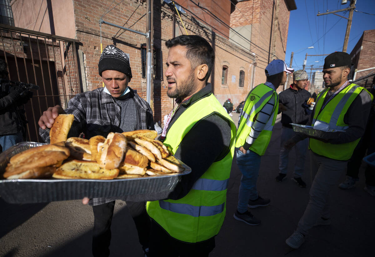 Church volunteers serve garlic bread to migrants camping outside the Sacred Heart Church in dow ...