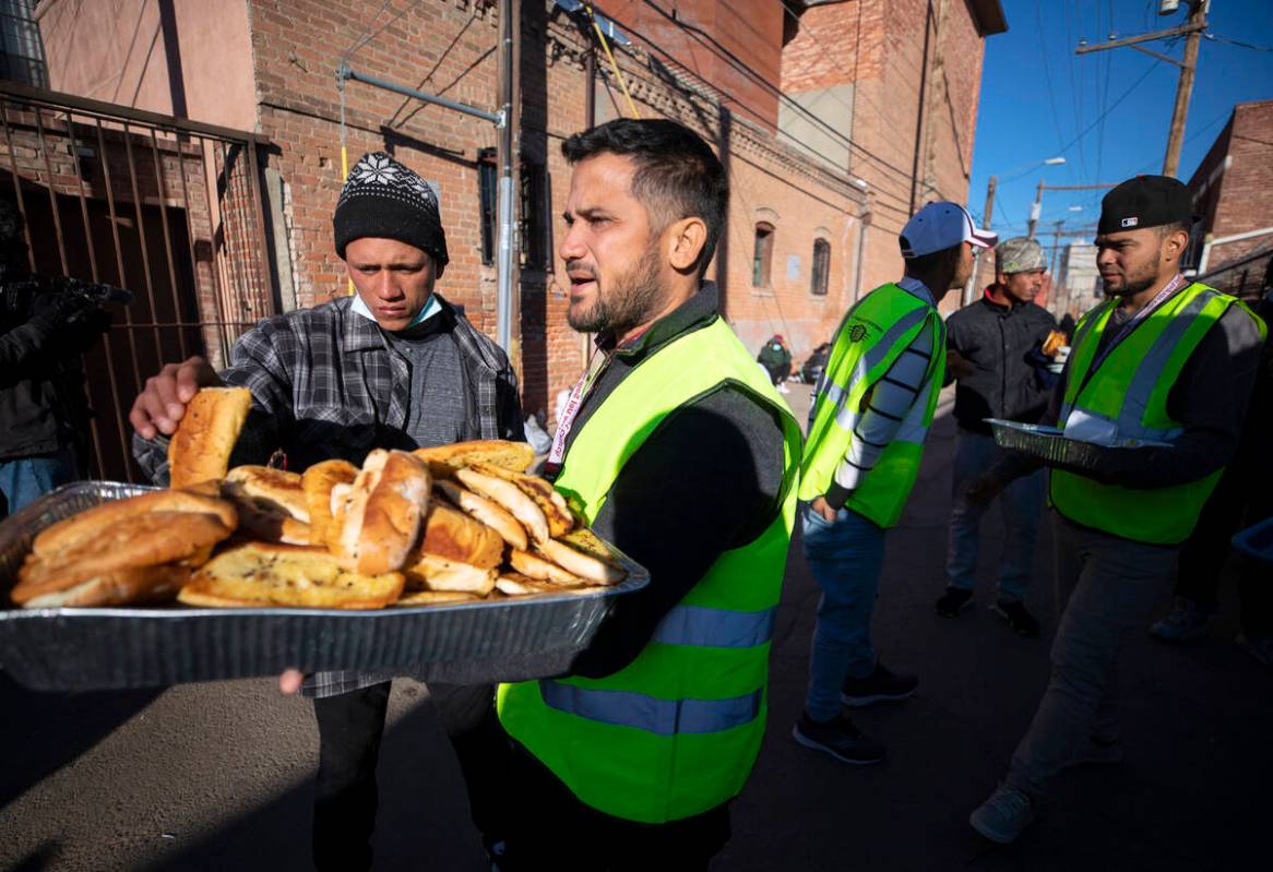 Church volunteers serve garlic bread to migrants camping outside the Sacred Heart Church in dow ...