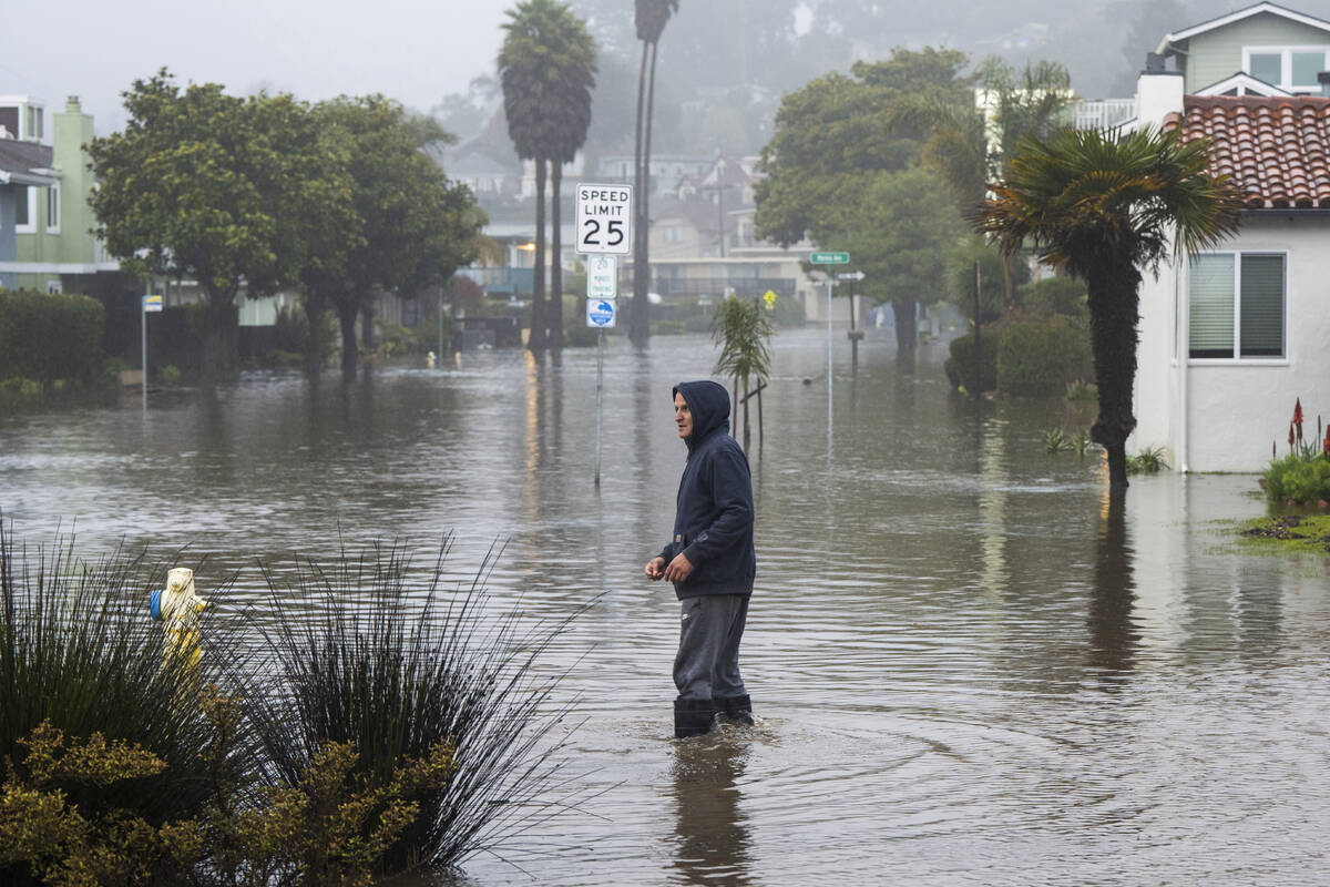 A man wades through a flooded street in the Rio Del Mar neighborhood of Aptos, Calif., Monday, ...