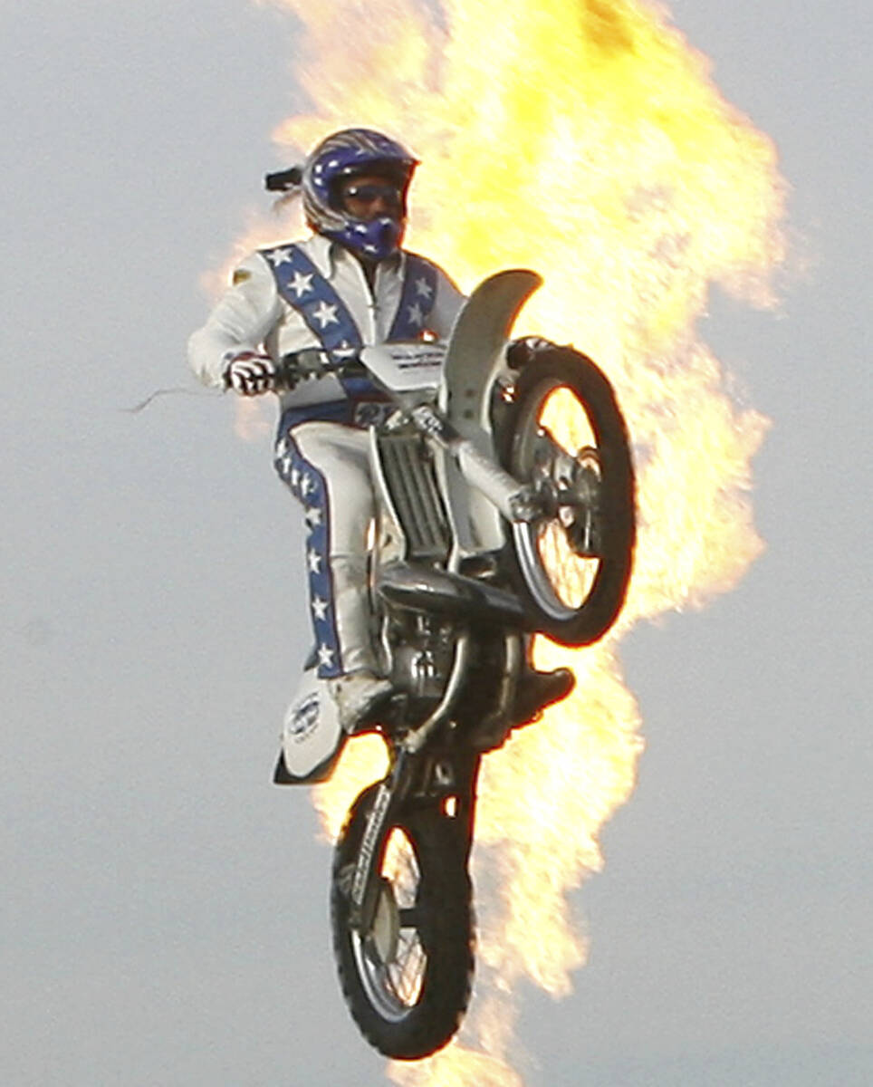 Daredevil Robbie Knievel is backlit in flames as he jumps over 24 delivery trucks, a 200 foot g ...