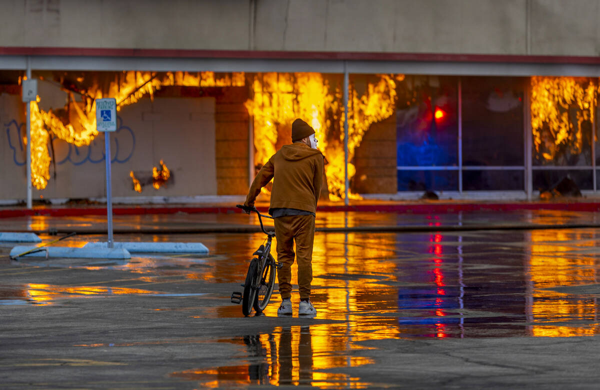 A masked bicycle rider looks on close by as Las Vegas and Clark County Firefighters work a full ...