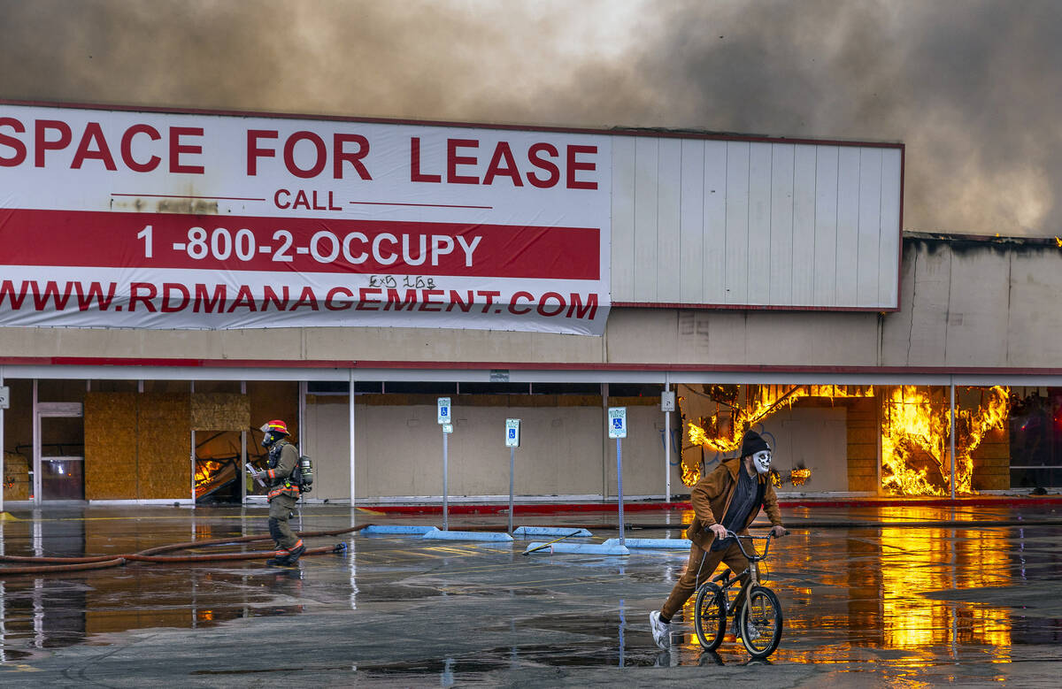 A masked bicycle rider rides close by as Las Vegas and Clark County Firefighters work a fully i ...