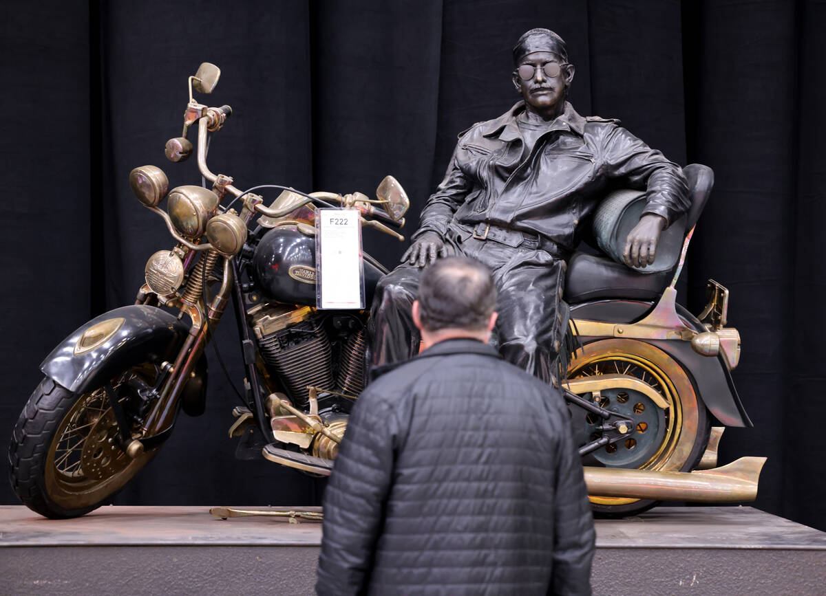 A bidder checks out a Bill Mack life-size bronze statue called “Taking a Break” a ...