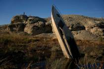A man stands on a hill overlooking a formerly sunken boat standing upright into the air with it ...