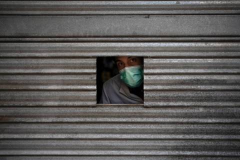 A man wearing a face mask looks out from a small opening on the door of a pharmacy as he waits ...