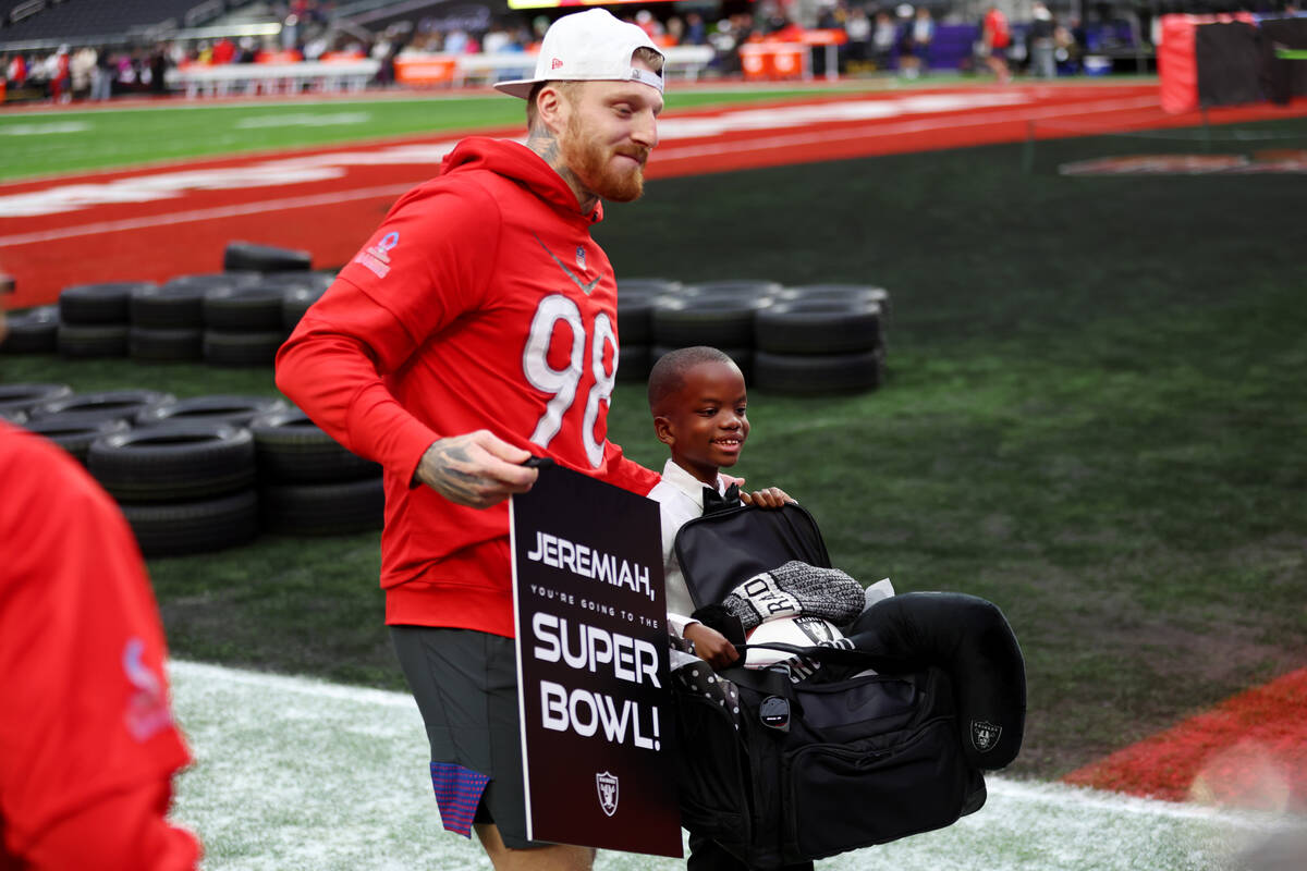 Jeremiah Fennell, 10, right, is surprised by Las Vegas Raiders defensive end Maxx Crosby (98) w ...