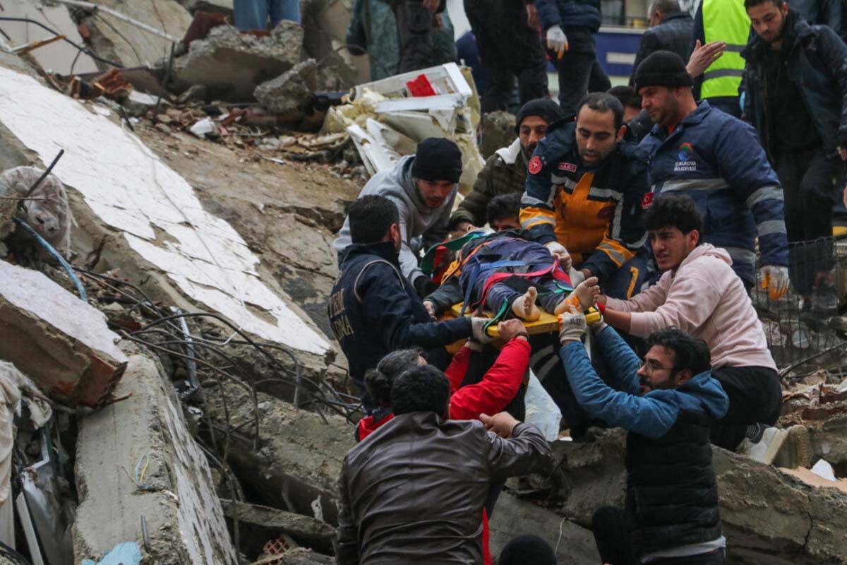 People and emergency teams rescue a person on a stretcher from a collapsed building in Adana, T ...