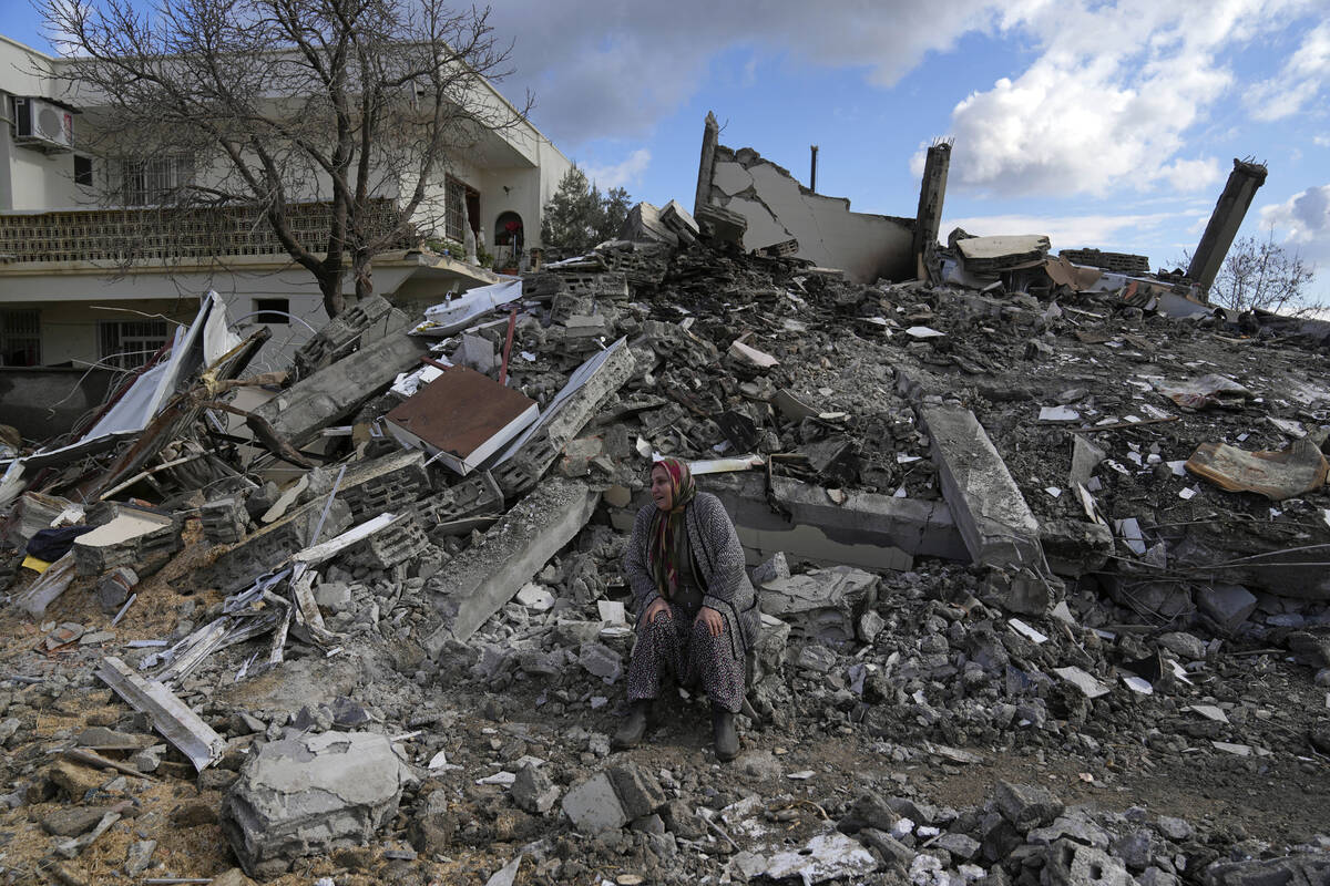 A woman sits on the rubble as emergency rescue teams search for people under the remains of des ...