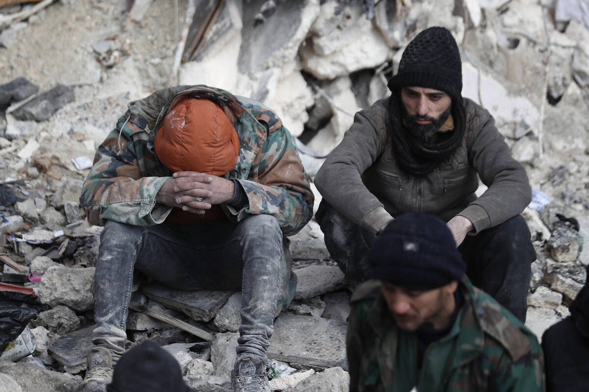 People react as they sit on the wreckage of collapsed buildings, in Aleppo, Syria, Tuesday, Feb ...