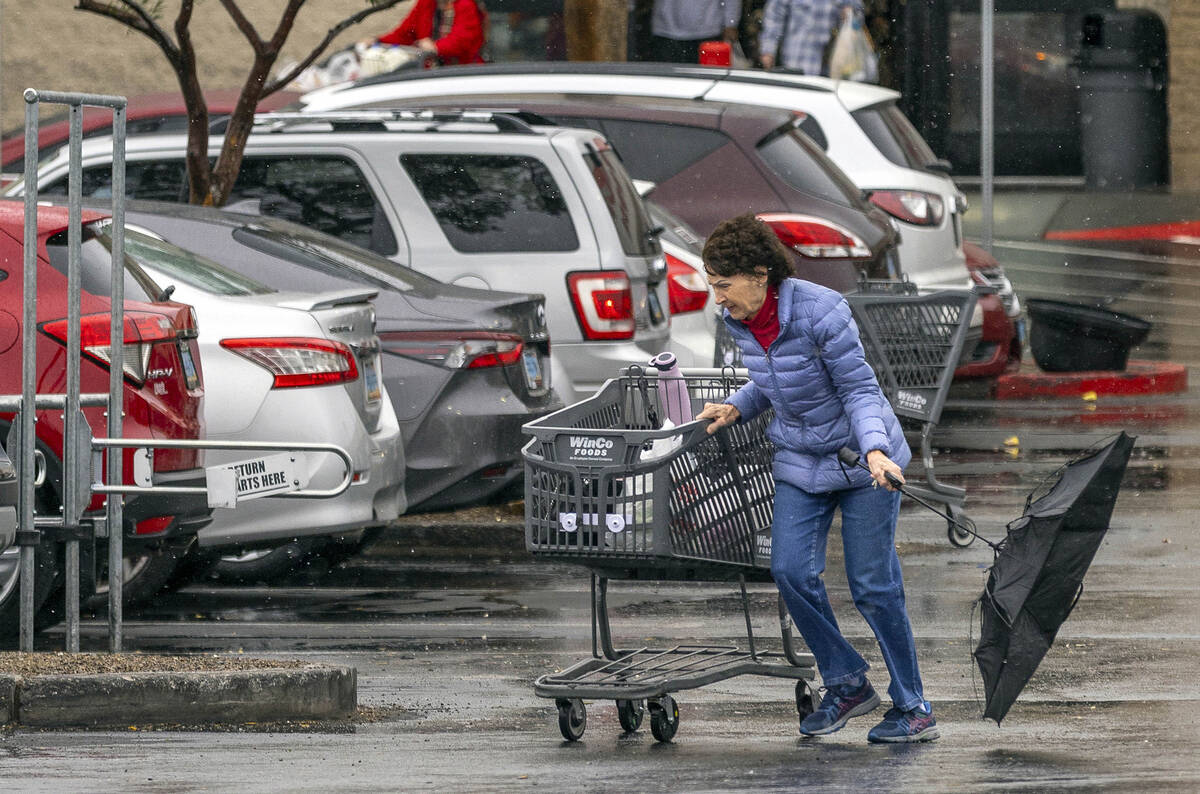 A customer braces against the weather with her umbrella flipping up while leaving WinCo Foods a ...