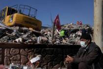 A man sits next to the rubble of destroyed buildings in Adiyaman, southern Turkey, Sunday, Feb. ...
