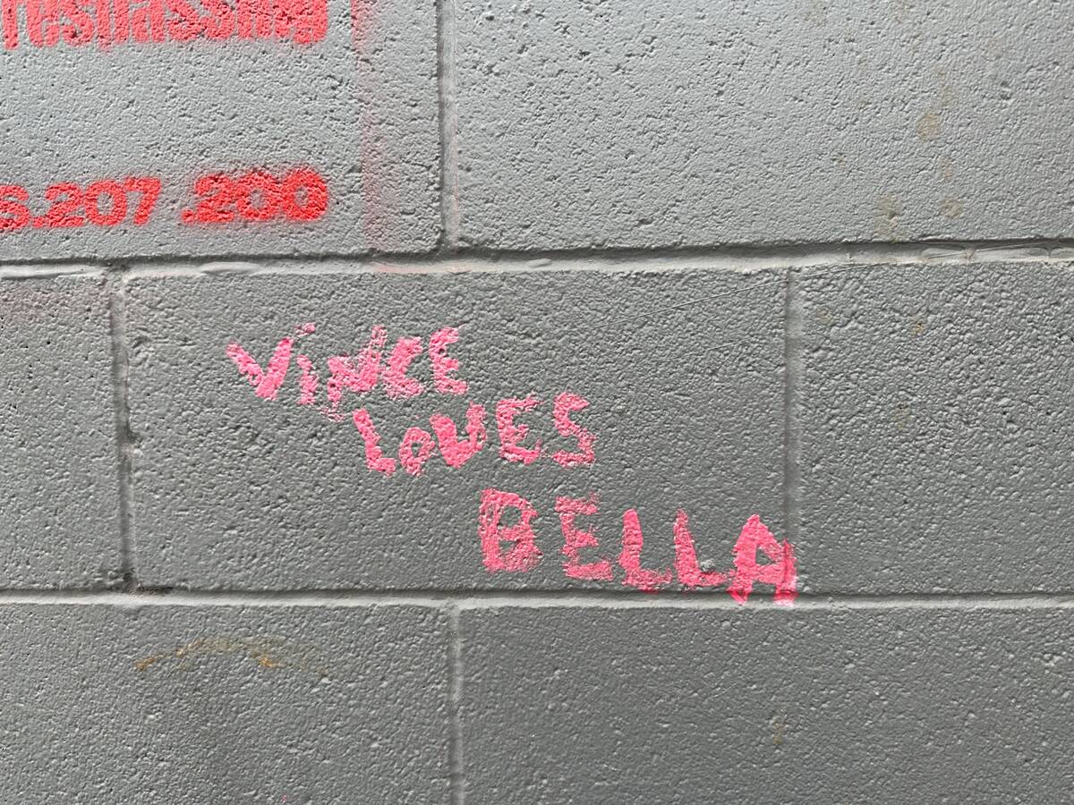 The words "VINCE LOVES BELLA" are visible on a wall near a makeshift encampment where police an ...