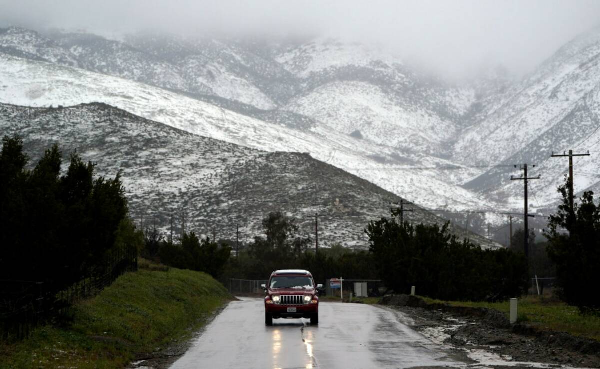 A motorist drives on a wet road under a snow-covered hillside Friday, Feb. 24, 2023, in Agua Du ...