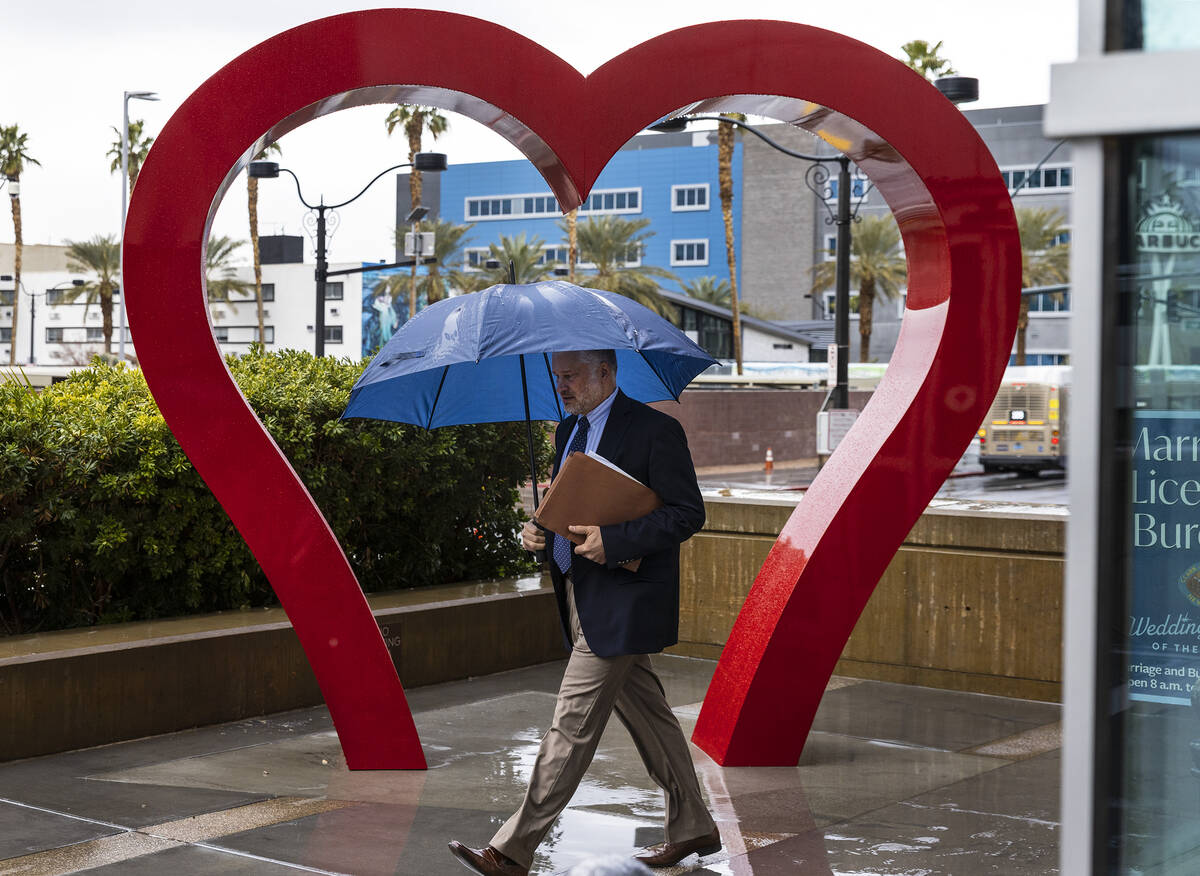 A pedestrian holds an umbrella to protect himself from rain as he walks past a giant heart scul ...