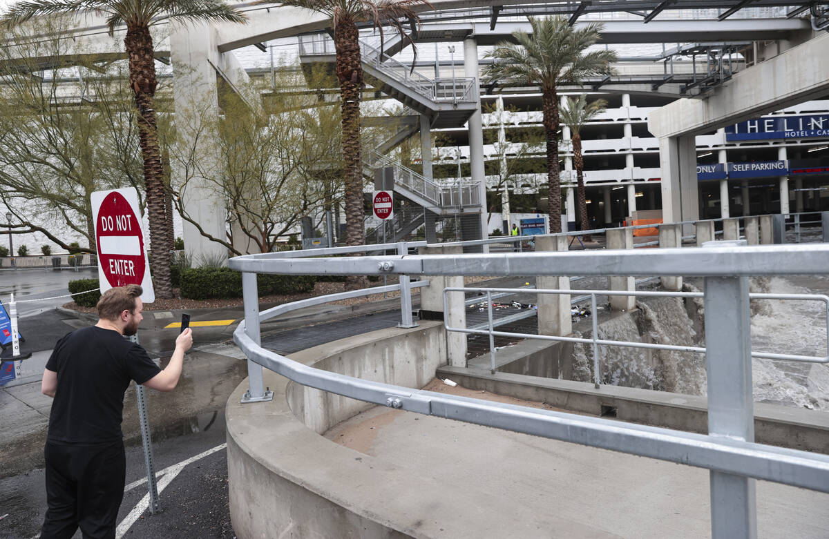 A man takes a picture as water flows from The Linq parking garage to a flood channel after rain ...