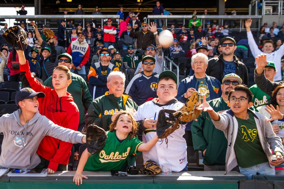 Fans berebut posisi untuk menangkap bola yang dilempar oleh pemain Oakland Athletics selama Liga Besar…