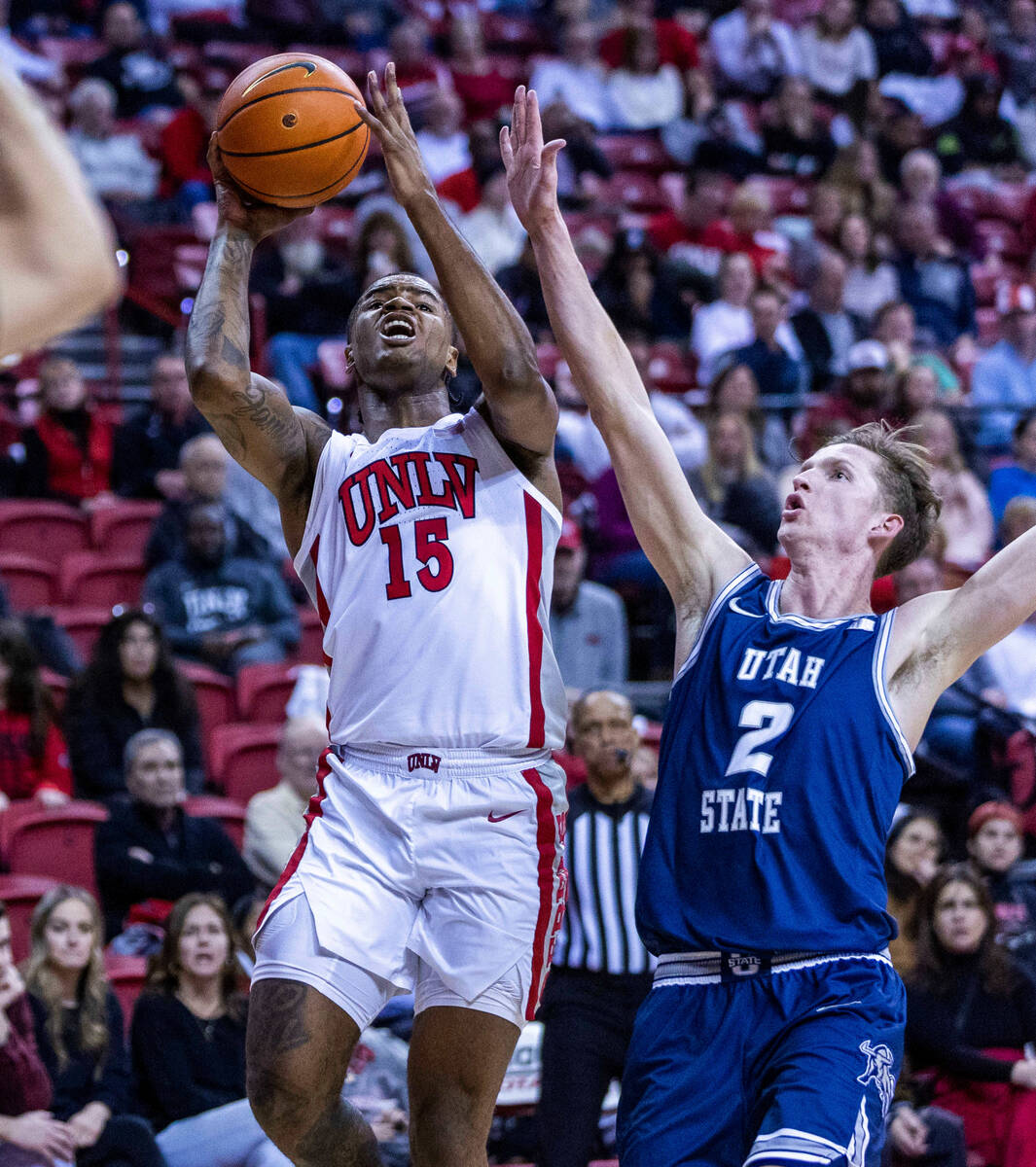 UNLV guard Luis Rodriguez (15) absorbs some contact and still shoots over Utah State guard Sean ...