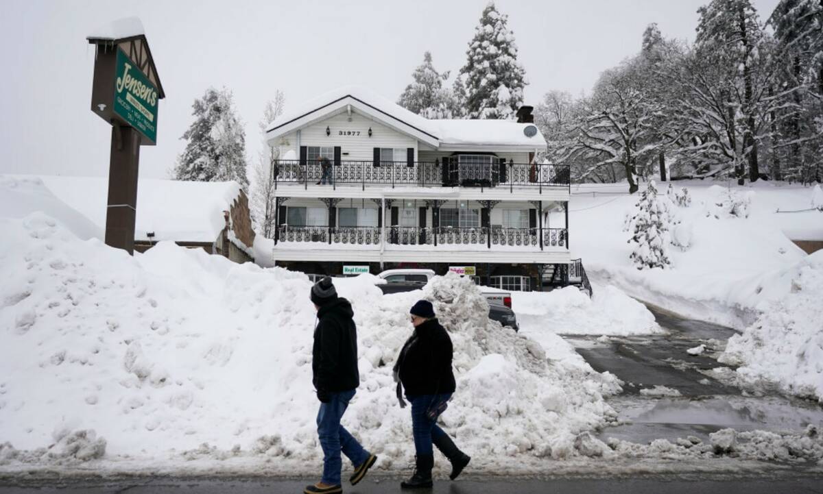 Two residents walk past the piles of snow in Running Springs, Calif., Tuesday, Feb. 28, 2023. ( ...