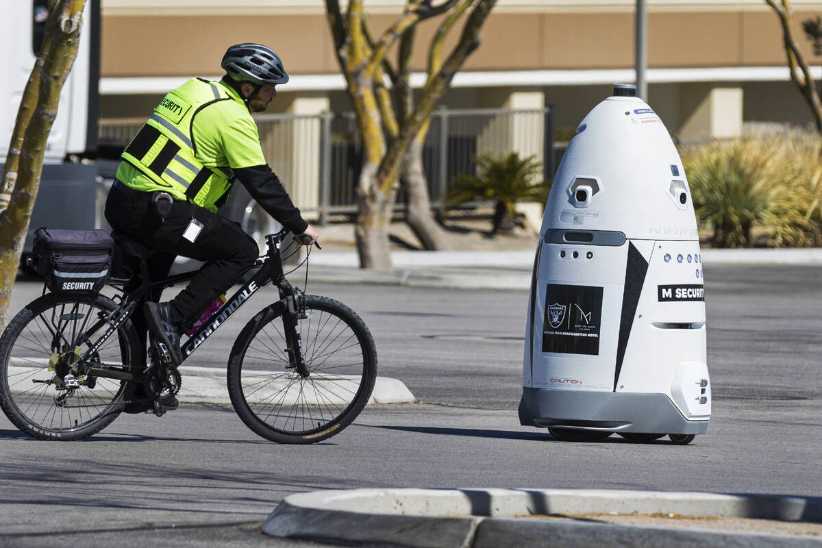 An M Resort security guard rides past an autonomous, human-sized robot, M Bot, as it patrols M ...