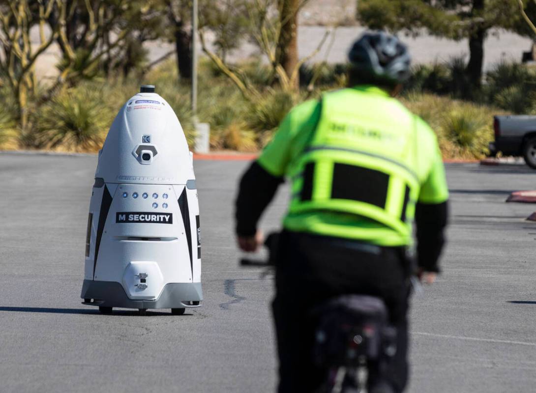 An M Resort security guard rides his bike toward an autonomous, human-sized robot, M Bot, as it ...