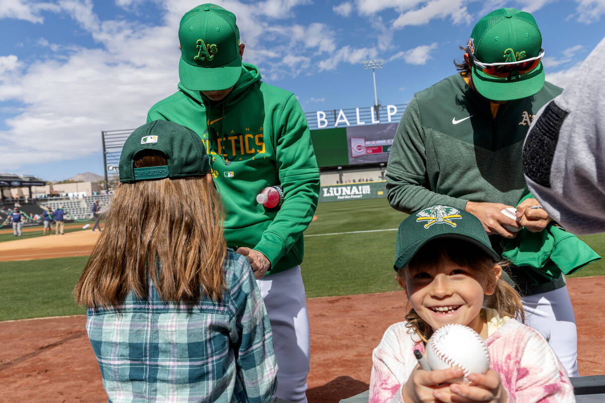 Indie Erardy, 7, shows off her autographed ball while Oakland Athletics players sign more balls ...