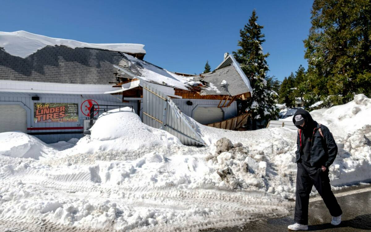 A man walks past a damaged tire shop in Crestline, Calif., Friday, March 3, 2023, following a h ...