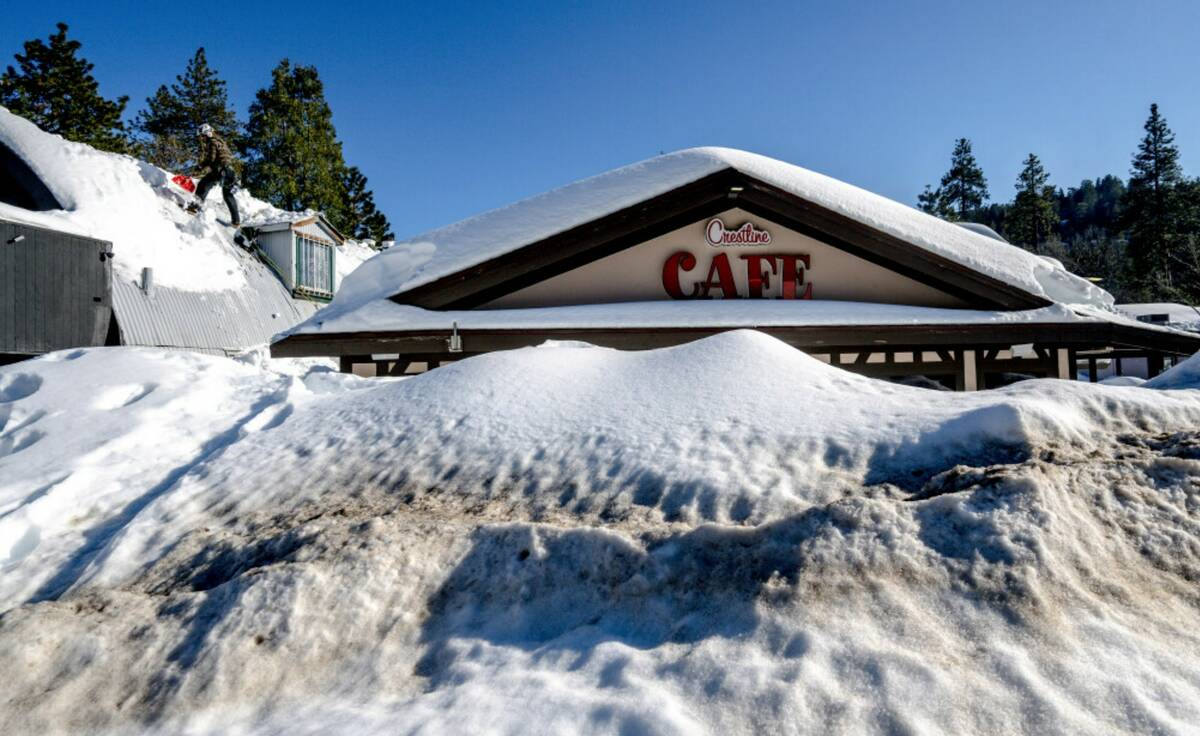 A man shovels snow off the roof of a store in Crestline, Calif., Friday, March 3, 2023, as buil ...