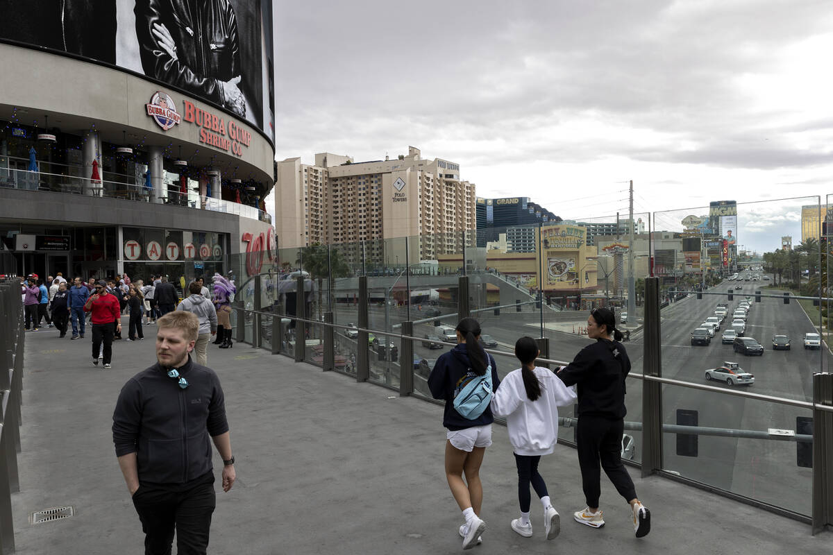 Pedestrians cross Las Vegas Boulevard next to Harmon Corner, left, a retail complex at the inte ...