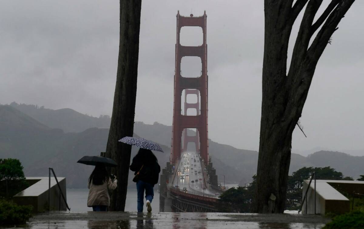 Traffic moves on the Golden Gate Bridge as people carry umbrellas while walking down a path at ...