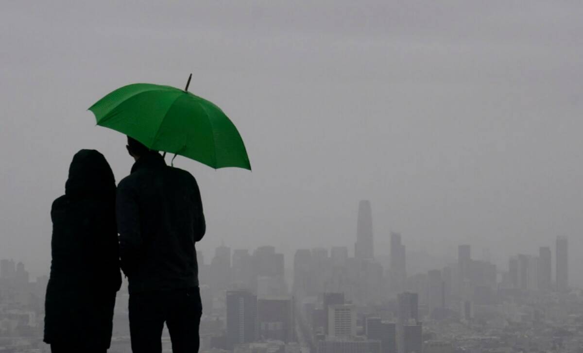 People stand under an umbrella while looking toward the skyline from Twin Peaks in San Francisc ...
