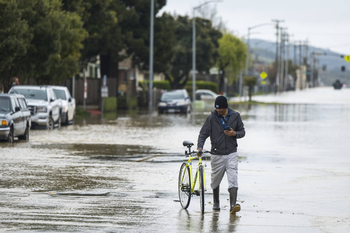 A man walks his bicycle through floodwaters in Watsonville, Calif., Saturday, March 11, 2023. ...