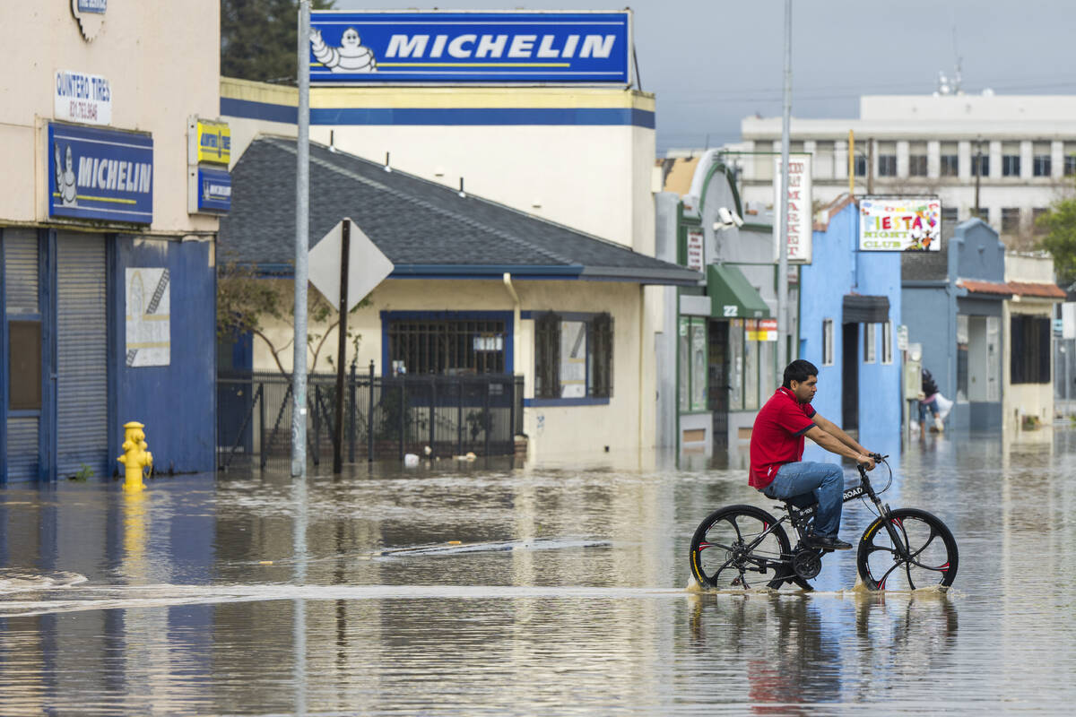 A man rides his bicycle through floodwaters in Watsonville, Calif., Saturday, March 11, 2023. ...