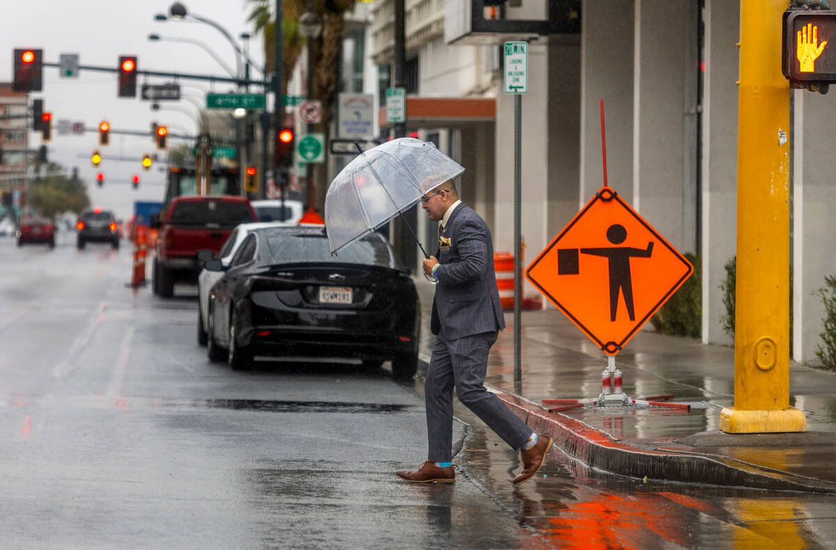 A pedestrian keeps dry under his umbrella as he walks along South 3rd St. as a storm system mov ...